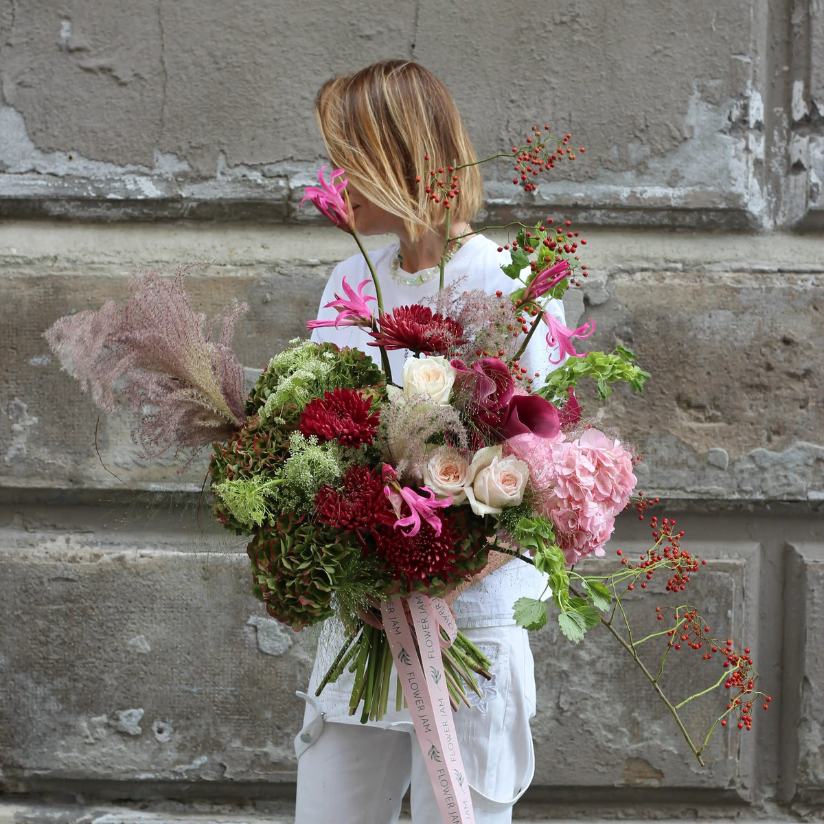 A woman dressed in white holding a bouquetin green and pink olours. A perfect mix of hydrangea, calla, roses, gerbera, clematis and some goodies.
