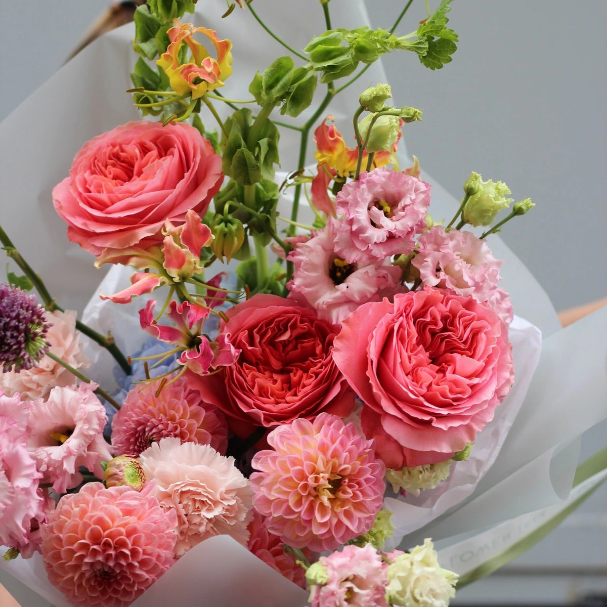 A close up of a bouquet made of english pink garden roses, pink dahlias and pink lisianthus and dianthus.