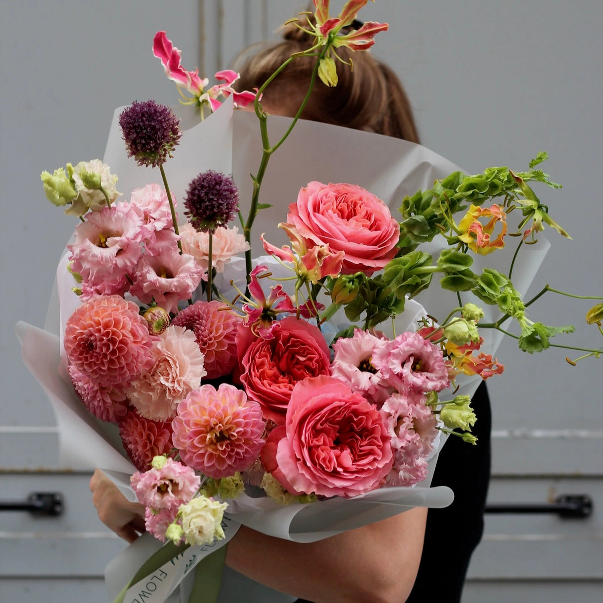 Pink gloriosa, pink lisianthus, pink english garden rose, purple  blue and green goodies, put together into a bouquet wrapped by neutral white paper