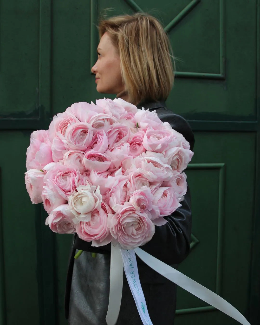 Woman holding a large bouquet of pink roses against a green door.