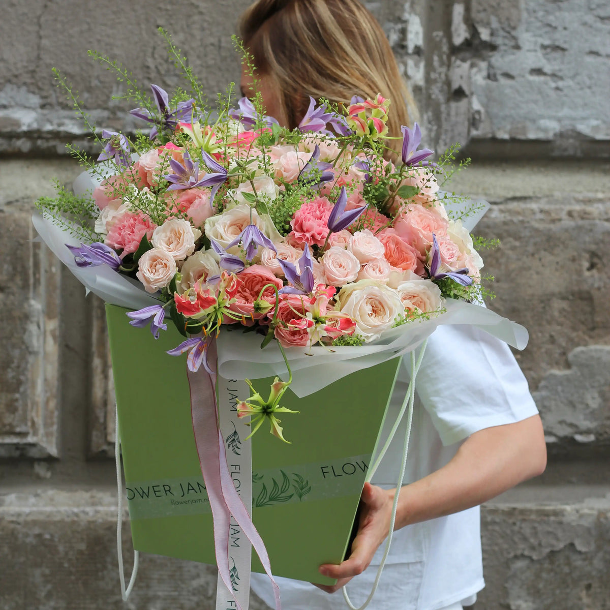 A green transportation box with a big colorful bouquet of pink roses, pink carnations, purple clematis and pinkk gloriosa.