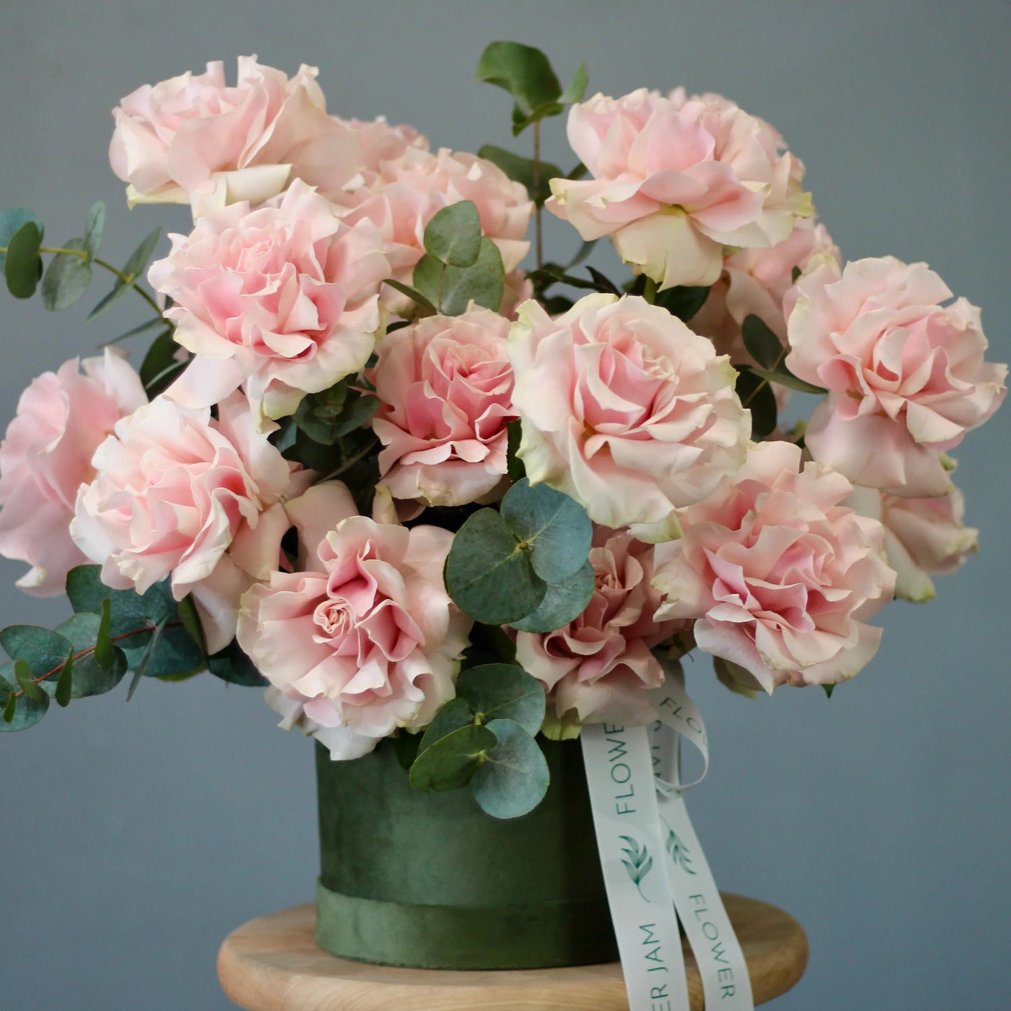 Bouquet of pink roses with green leaves in a green vase on a gray background
