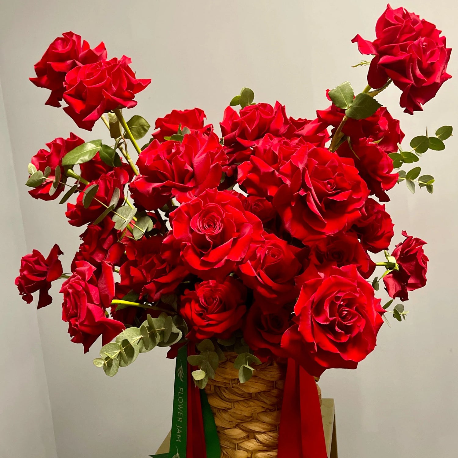 Bouquet of red roses with a woven basket and green ribbon on a neutral background